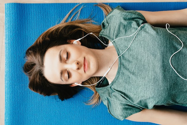 Tranquil woman resting on yoga mat in earphones at home