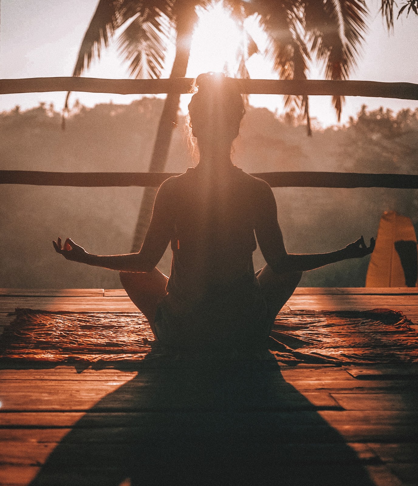 A woman sits in lotus position to practice meditation in front of a sunset to adjust to life after quarantine